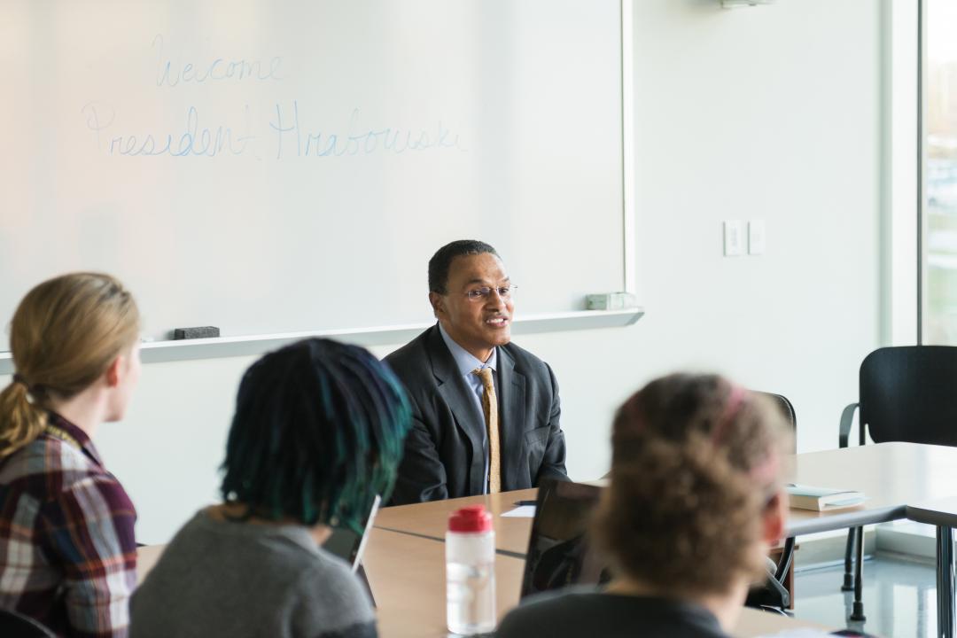 UMBC总裁Freeman Hrabowski博士与三个学生一起坐在桌子旁